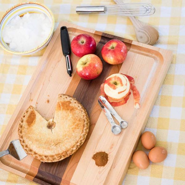 Apples peeled and an apple tart on a striped designer cutting board