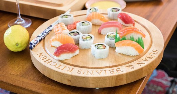Sushi sits on a round cutting board engraved with text "Susan & Brian's Kitchen"